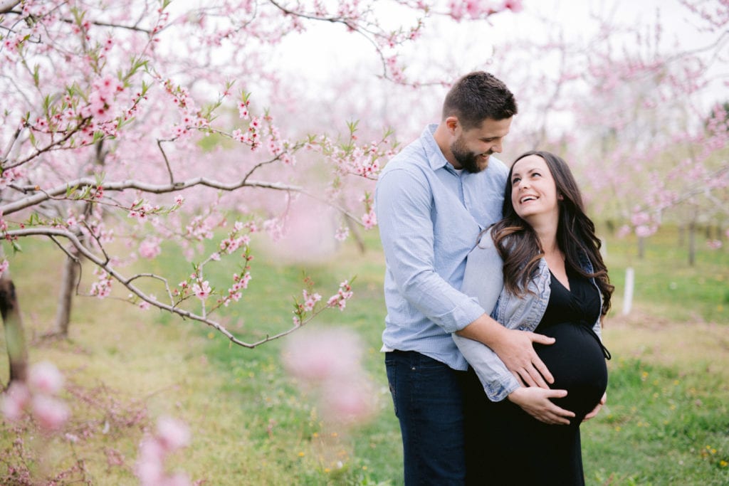 Pregnant Couple Looking at each with love during maternity photos in pink blooms in spring by Niagara Photographer
