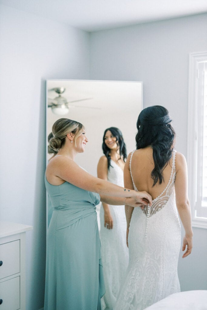 Bride putting wedding dress on with help of maid of honour