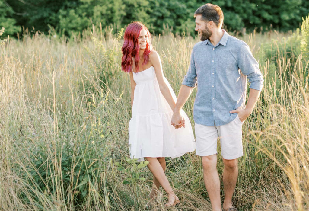 Engaged Couple Walking Through A field at sunset in Niagara on the lake taken by St. Catharines Wedding Photographer