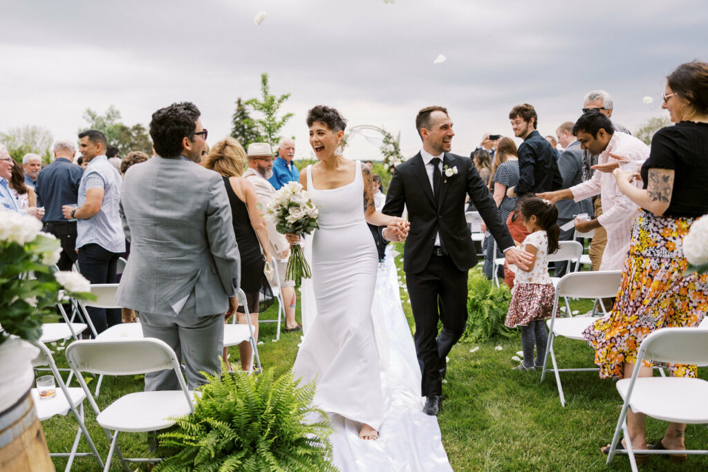 Bride & Groom walking out of ceremony while guests throw flowers both filled with joy taken by Niagara Wedding Photographer