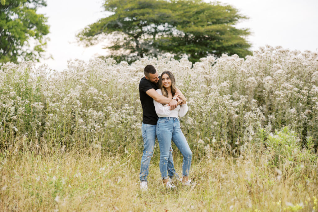 Engaged Couple in field in the summer time looking happy at golden hour in Niagara on the lake by Ontario Luxury Wedding Photographer